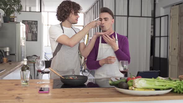 Young Gay Couple Cooking and Tasting Delicious Healthy Food Cooking in the Kitchen alt