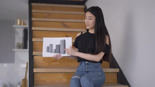 Portrait of Young Confident Asian Woman Posing with Business Graph in Home Office alt