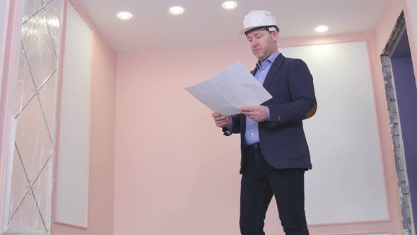 Senior Engineer In Hardhat Is Standing And Looking At A Blueprint