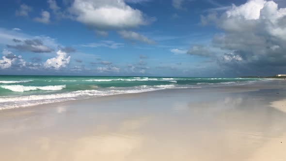 Slow motion camera pan along caribbean white sandy beach with cloud formations alt