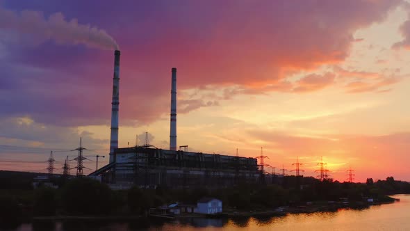 Factory chimneys smoke on the river bank in the evening alt