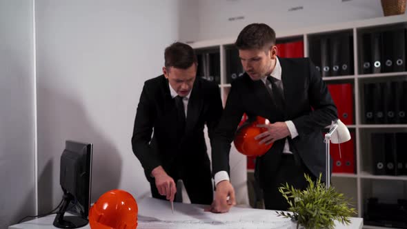 Two Engineers Businessmen in Business Office Look at Architect Drawing with Helmet alt