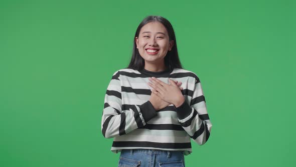 Proud Asian Woman Touching Her Chest While Standing In Front Of Green Screen Background alt