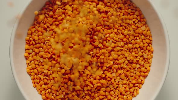 Red lentils grains falling into a white bowl