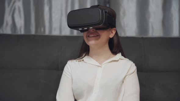 Portrait of Young Smiling Woman Wearing Virtual Reality Glasses Sitting on Sofa at Home. Concept Vr