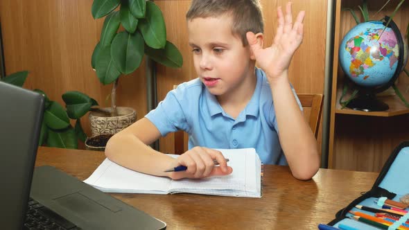 A 7Yearold Schoolboy Writes and Shows a Notebook to the Monitor