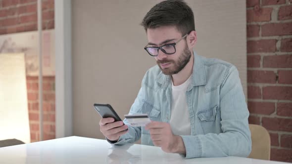 Young Male Designer Making Online Payment on Smartphone alt