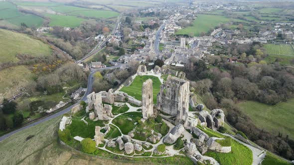 Aerial tilt down forward over Corfe Castle ruins and village in background. England alt