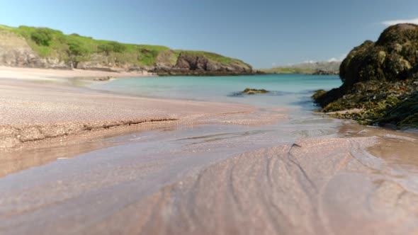 Close up shot of water steadily flowing across a beach and into a turquoise ocean, eroding the sand alt