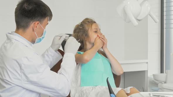 Young Girl Refusing Showing Teeth To a Dentist Covering Her Mouth with Her Hands