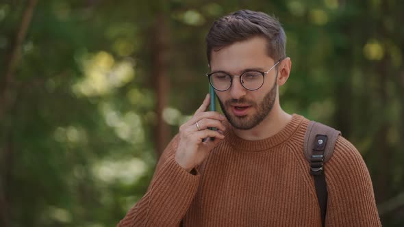 A Male Traveler with a Backpack Walks Through the Forest and Talks on a Mobile Phone in Slow Motion alt
