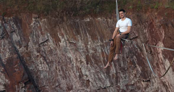 Slackliner is Sitting on the Rope Smiling and Flipping Off alt