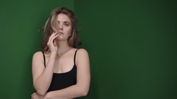 Blonde Woman Touches Her Hair and Body Wearing a Bodysuit in Green Studio