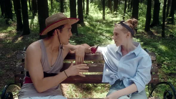 A Guy in a Straw Hat and a Girl in a Blue Shirt Chat Sitting on a Park Bench