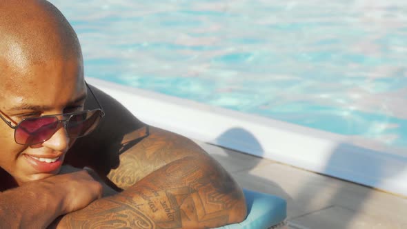 Sliding Shot of a Happy African Man Enjoying Sunbathing By the Swimming Pool
