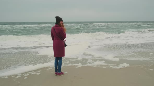 Lonely Girl Stands Near the Sea White Foam on the Shore of the Cold Winter Sea on a Foggy Day