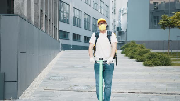 Delivery Man with Yellow Backpack and Protective Mask Riding Electric Scooter alt