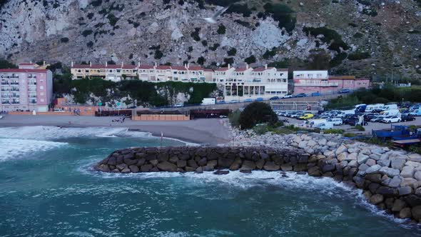 Turquoise Beach With Crashing Waves Onto Sea Walls On Catalan Bay In Gibraltar. Aerial Pullback alt
