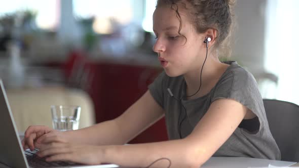 Female Student with Headphones in Her Ears is Typing on a Laptop Keyboard alt