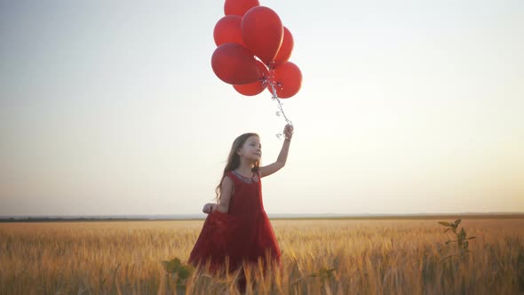 Happy Young Girl with Balloons Running in the Wheat Field at Sunset alt