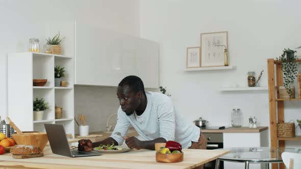 Afro-American Man Using Laptop and Eating Salad at Home alt