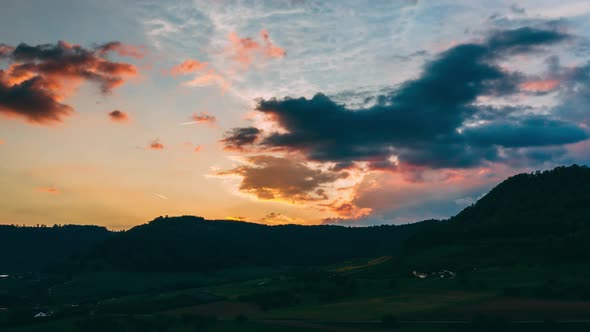 aerial hyperlapse at sunset over swiss countryside. dramatic moving clouds in sky with orange color alt