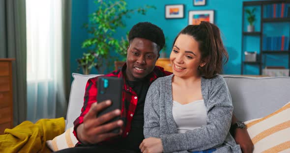 Man and Woman Making Video Call Taking Selfie Sitting on a Sofa Together at Home alt