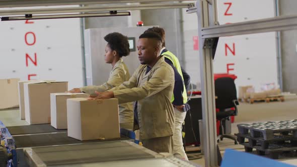 Diverse male and female workers with boxes on conveyor belt in warehouse alt