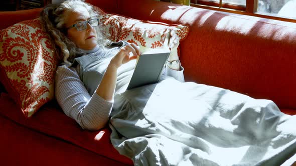 Mature woman reading a book in living room 4k alt