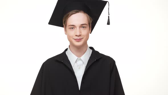 Young Caucasian Male Graduate in Black Robe and Square Academic Cap Standing on White Background alt
