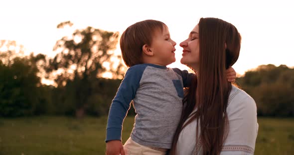 The Son Kisses His Mother Sitting at Sunset in a Field Hugging and Loving Mother alt