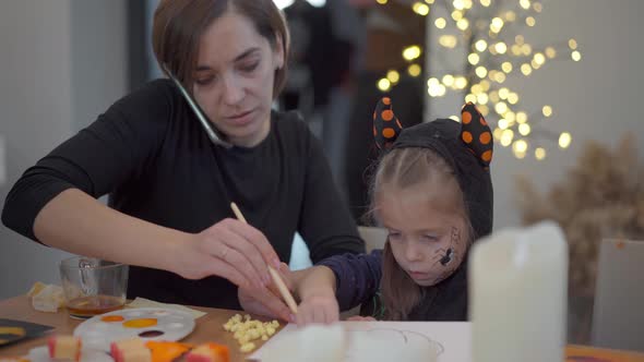 Little Girl Dressed Halloween Carnival Costume with Her Mother Sitting on the Table Drawing Handmade alt