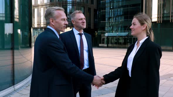 Two Businessmen Meet a Businesswoman and Shake Hands with Her, All Together Look at the Camera 