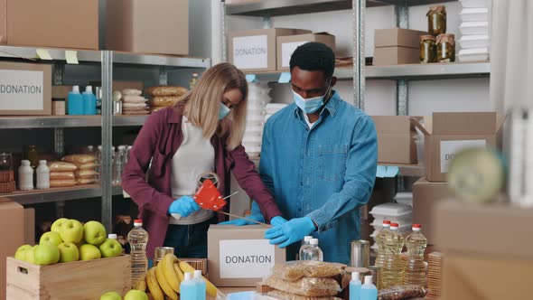 Diverse Volunteers in Face Masks Packing Boxes for Donation alt