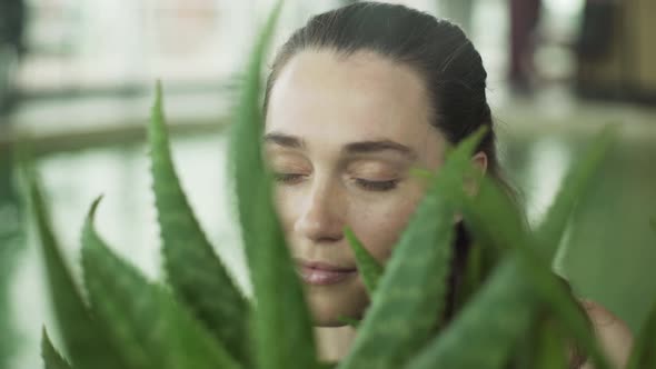 Young woman opening eyes and smiling through aloe vera plant