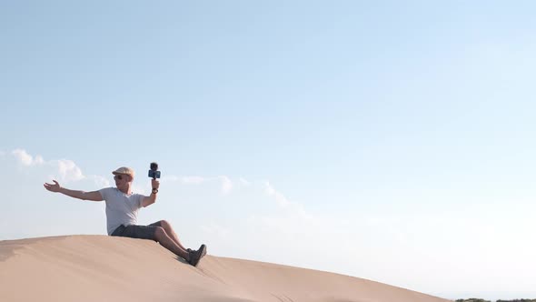 Man filming himself with his cell phone in the desert dunes. alt