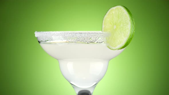 Classic Margarita cocktail on green background, rotate. Glass with a cocktail alt