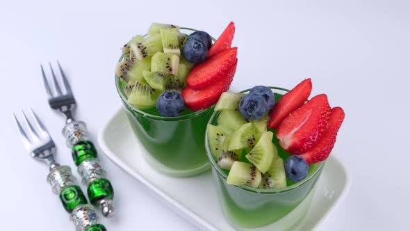 Two Fruit Jelly Green Desserts in Glasses with Kiwi Strawberries and Blueberries on a White