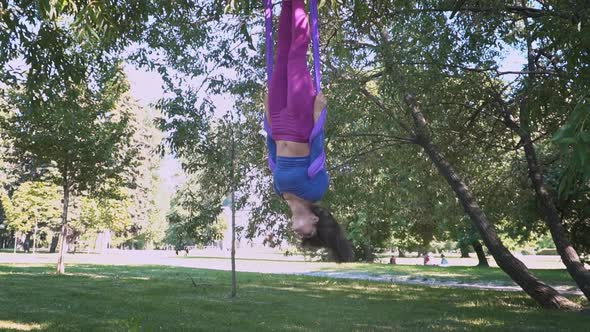 Young Beautiful Sportswear Woman Training Aero Stretch Swing Sunny City Park Hanging Upside Down alt