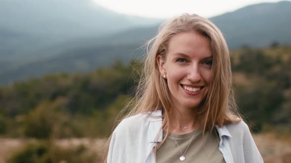 Young Smiling Blonde Woman Standing in Mountains Portrait