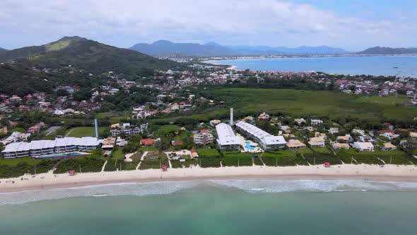 Aerial drone view of tourist beach with several summer houses facing the sea with lots of vegetation alt