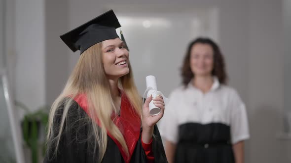 Happy Excited Graduate Posing with Rolled Diploma Looking Back at Blurred Woman alt
