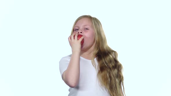Child Bites an Apple It Is Very Tasty. White Background. Slow Motion alt