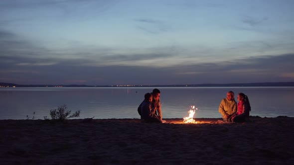 Family of Travelers with Kids Rest Around Night Campfire By Sea alt