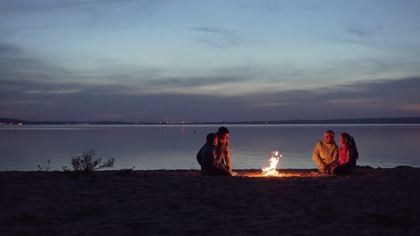 Family of Travelers with Kids Rest Around Night Campfire By Sea