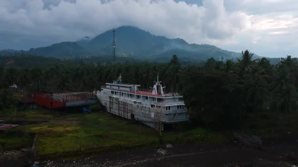 Aerial drone view of an abandoned cruise shipwreck on an isolated tropical island with a dormant vol alt