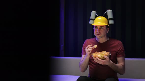 Funny Man With Beer Helmet on the Head Eating Chips While Watching Movie on the Sofa
