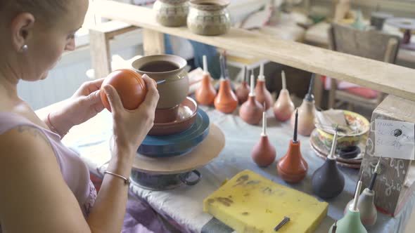 Female Potter Uses a Tool to Cover Clay Pot with Paint Working in Workshop alt