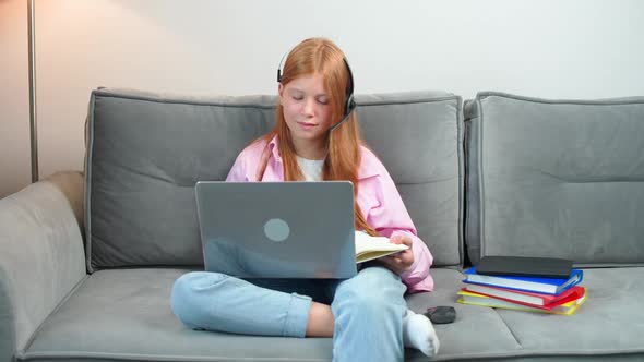 Distance Learning Redhaired Teen Girl Sitting on the Couch in Living Room and Uses a Laptop to Study alt
