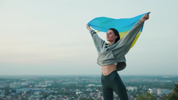Portrait of Beautiful Ukrainian Woman with Flag Unfurling in the Wind in Hands alt
